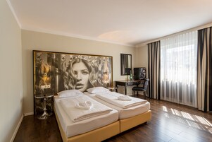Een hotelkamer met een groot bed, een bureau, een stoel, een grote spiegel en een raam met gordijnen.