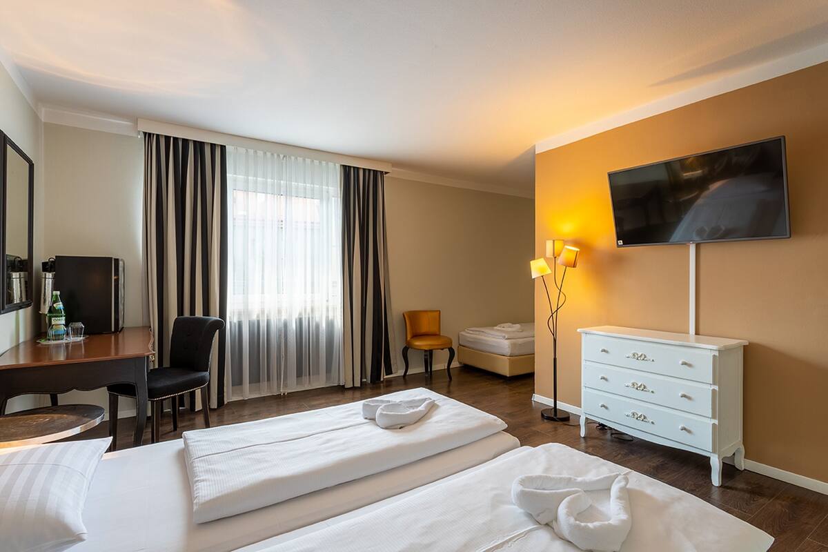 A hotel room with two beds, a desk, a chair, a TV, and a dresser.