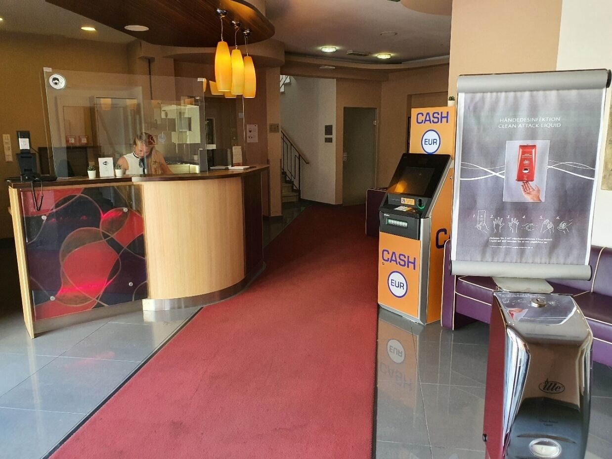 A hotel reception area with a red carpet, a wooden reception desk, and a cash machine.