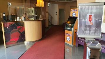 A hotel reception area with a red carpet, a wooden reception desk, and a cash machine.