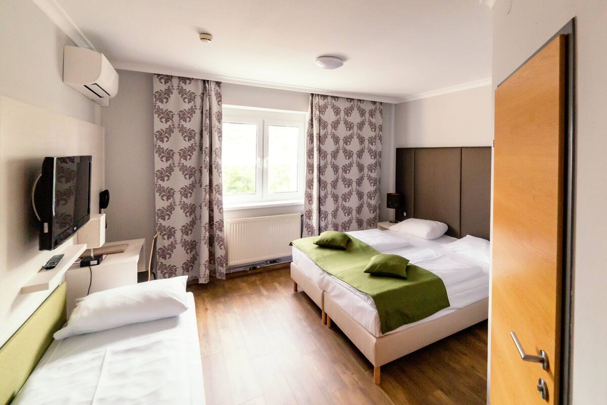 A hotel room with two beds, a television, a window with curtains, and a door.