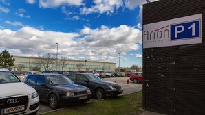 A parking area with several cars, a sign for Arion Airport Hotel, and a building in the background. - Arion Hotel Vienna Airport (Schwechat)