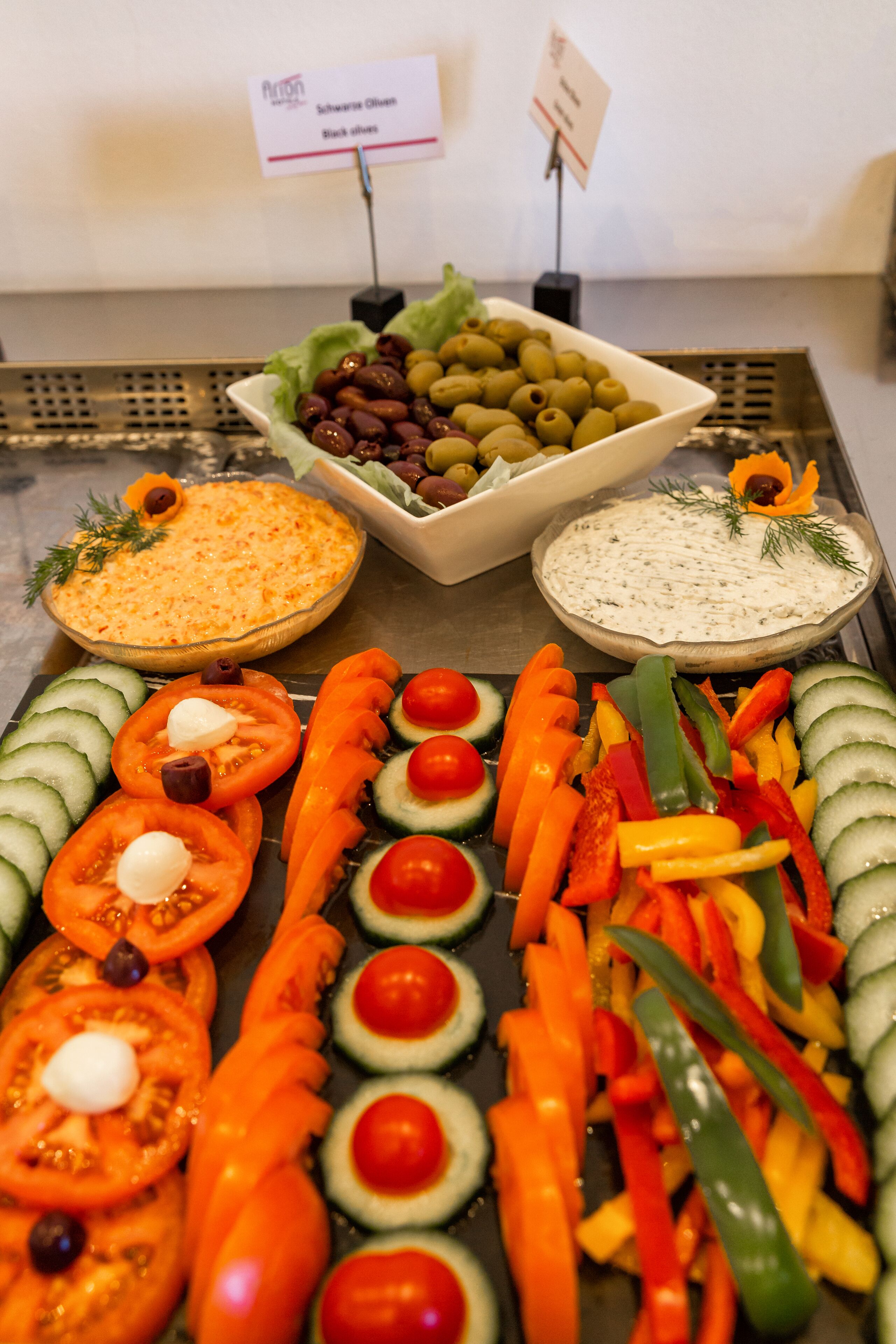 A buffet with various dishes including olives, sliced vegetables, and two types of dips.