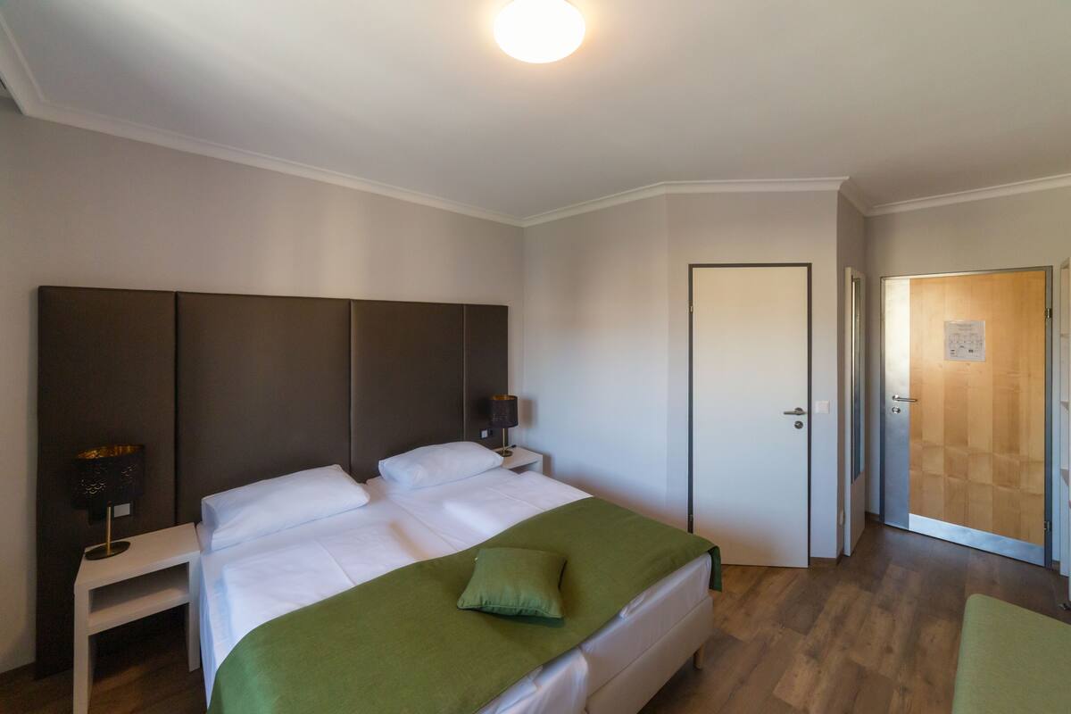 A bedroom with a large bed, bedside tables, a nightstand, and a door leading to another room.