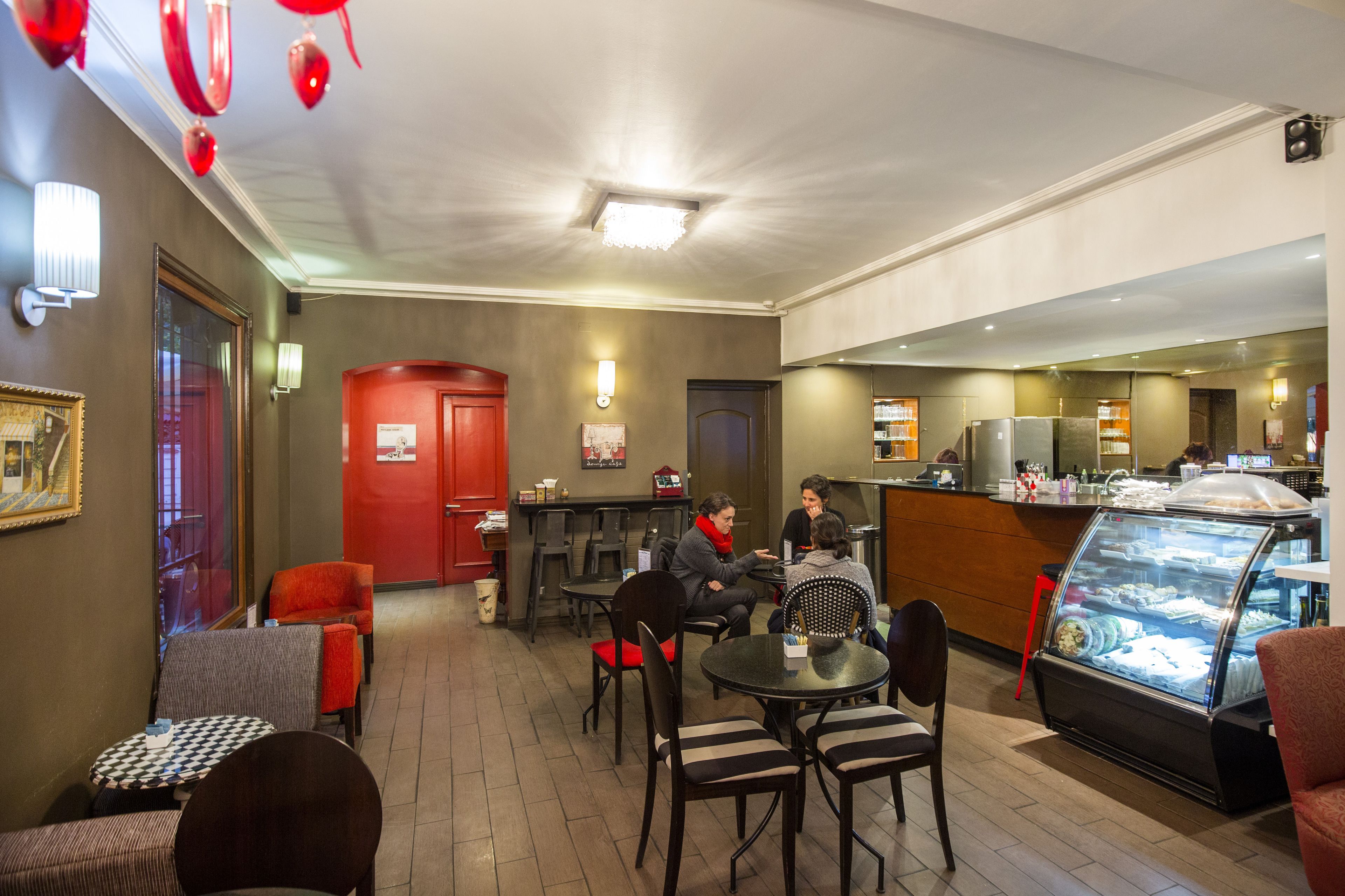 A cozy cafe with tables and chairs, a counter, and a display case with food items.