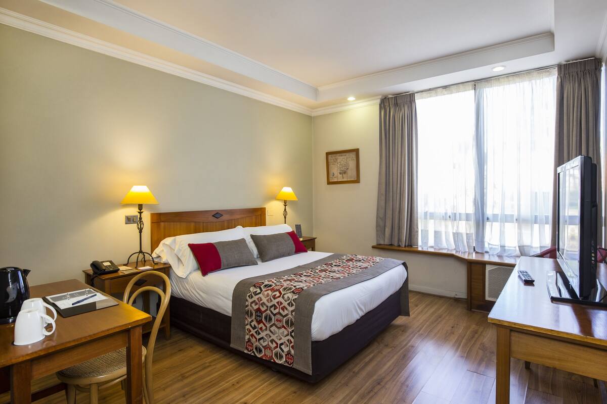 Une chambre d’hôtel comprenant un lit, des lampes de chevet, un bureau avec une machine à café, une télévision et une fenêtre avec des rideaux.