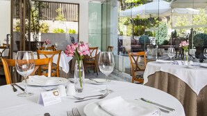 A dining area with tables set for two, featuring white tablecloths, clear glassware, and a vase with pink flowers. - Hotel Bonaparte Boutique (Santiago)