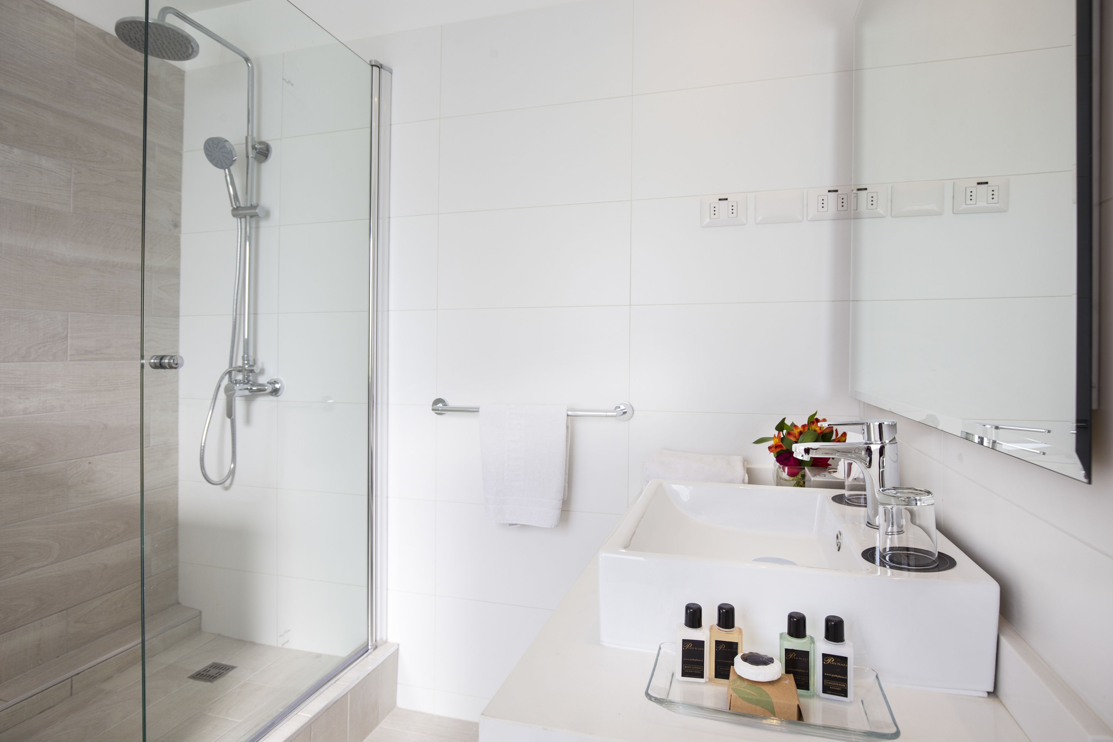 A modern bathroom with a glass-enclosed shower, a white sink with a mirror above, and a small vase with flowers on the countertop.