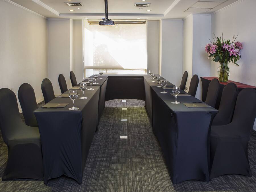 Ein Konferenzraum mit einem langen Tisch, schwarzen Stühlen und einem Blumenstrauß.