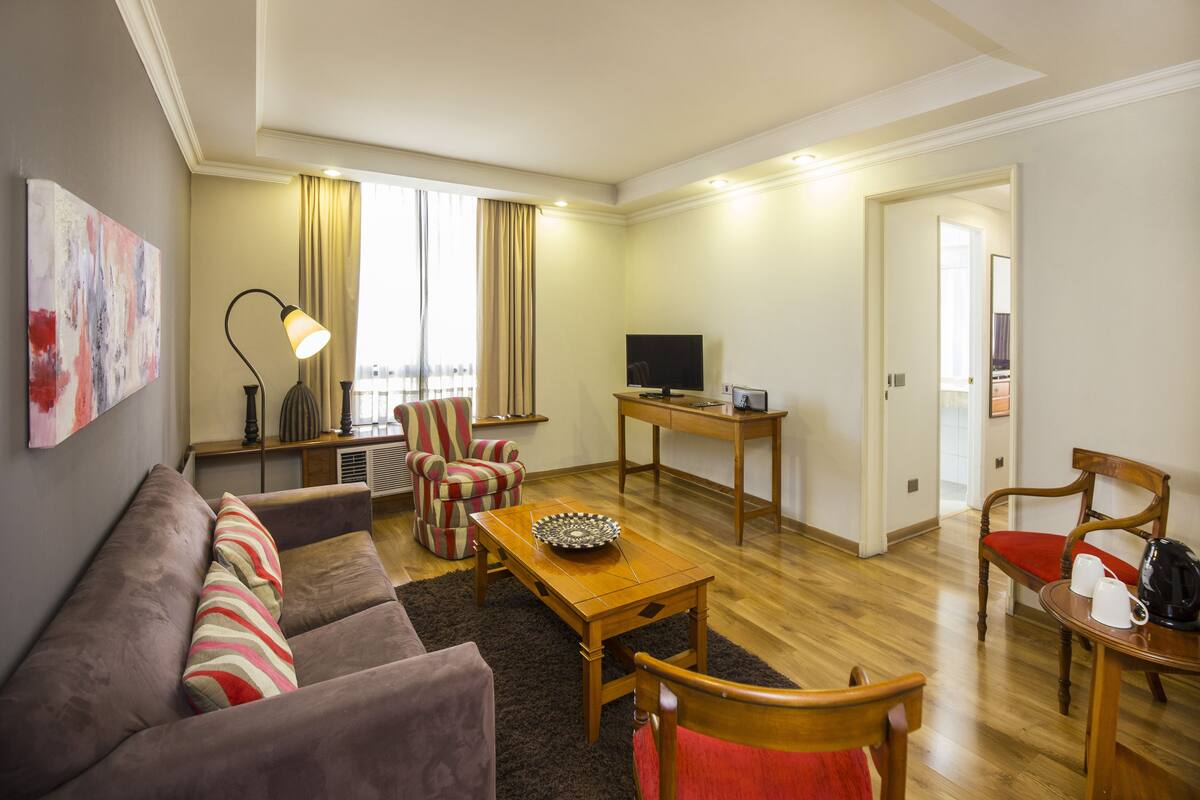 Un salon comprenant un canapé, un fauteuil, une table basse, un téléviseur et une petite table avec des tasses et une bouilloire.