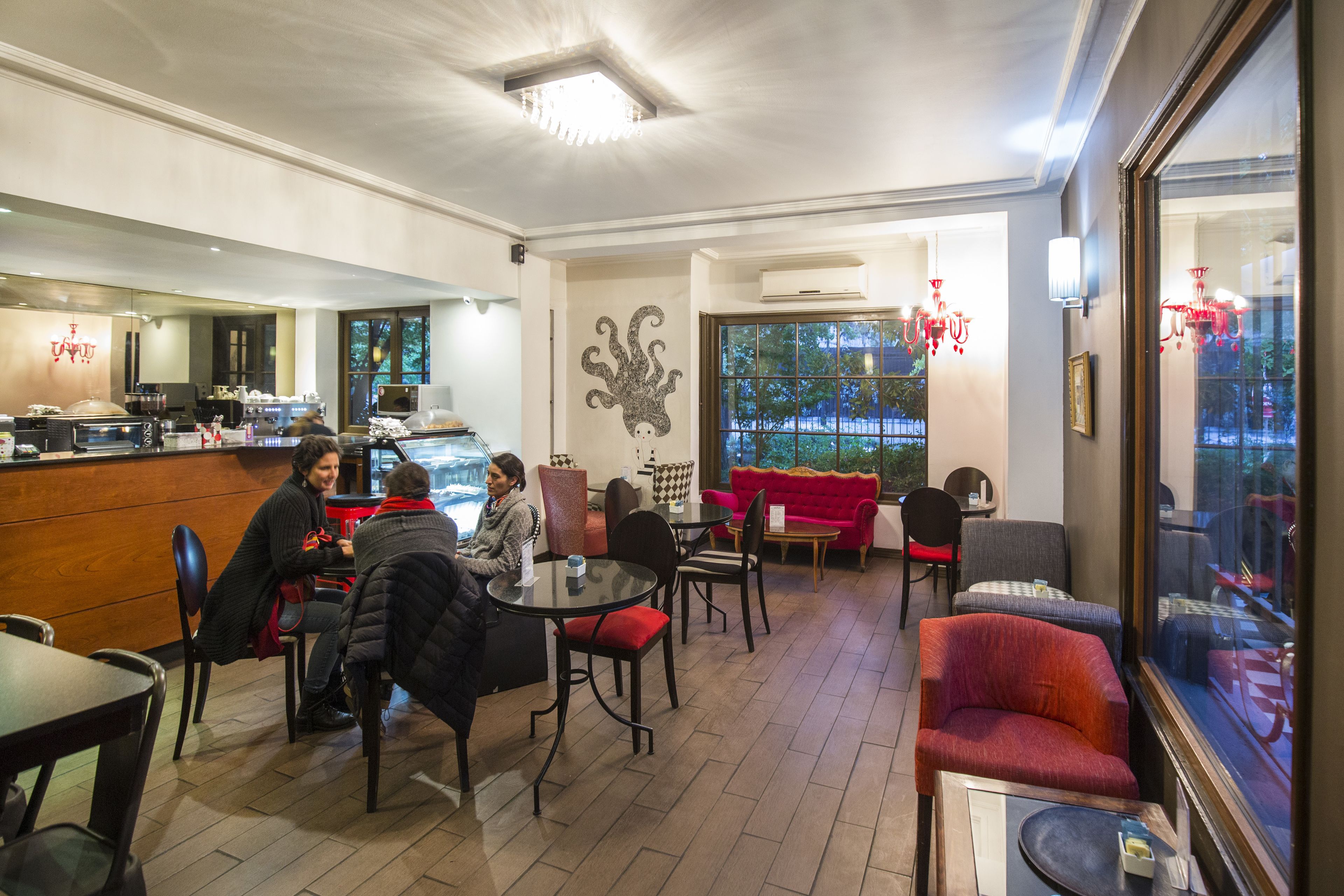 Un café acogedor con muebles de madera, un sofá rojo y un ventanal que ofrece vistas al exterior.