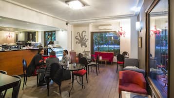 Un café acogedor con muebles de madera, un sofá rojo y un ventanal que ofrece vistas al exterior.