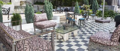 A checkered outdoor patio with vintage furniture, including a glass-top table and patterned sofas.
