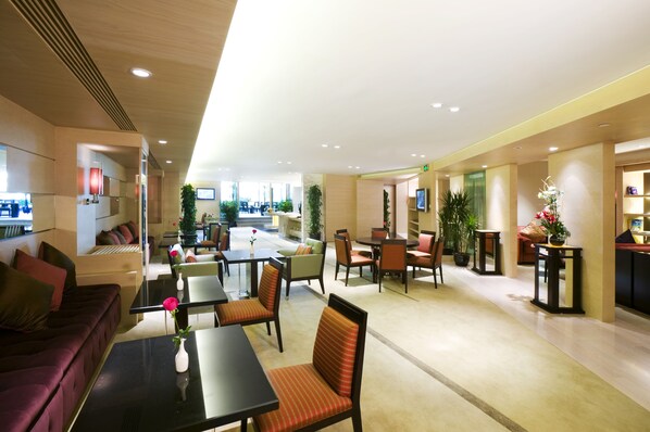 A hotel lobby with seating areas, a reception desk, and a staircase leading to other floors.