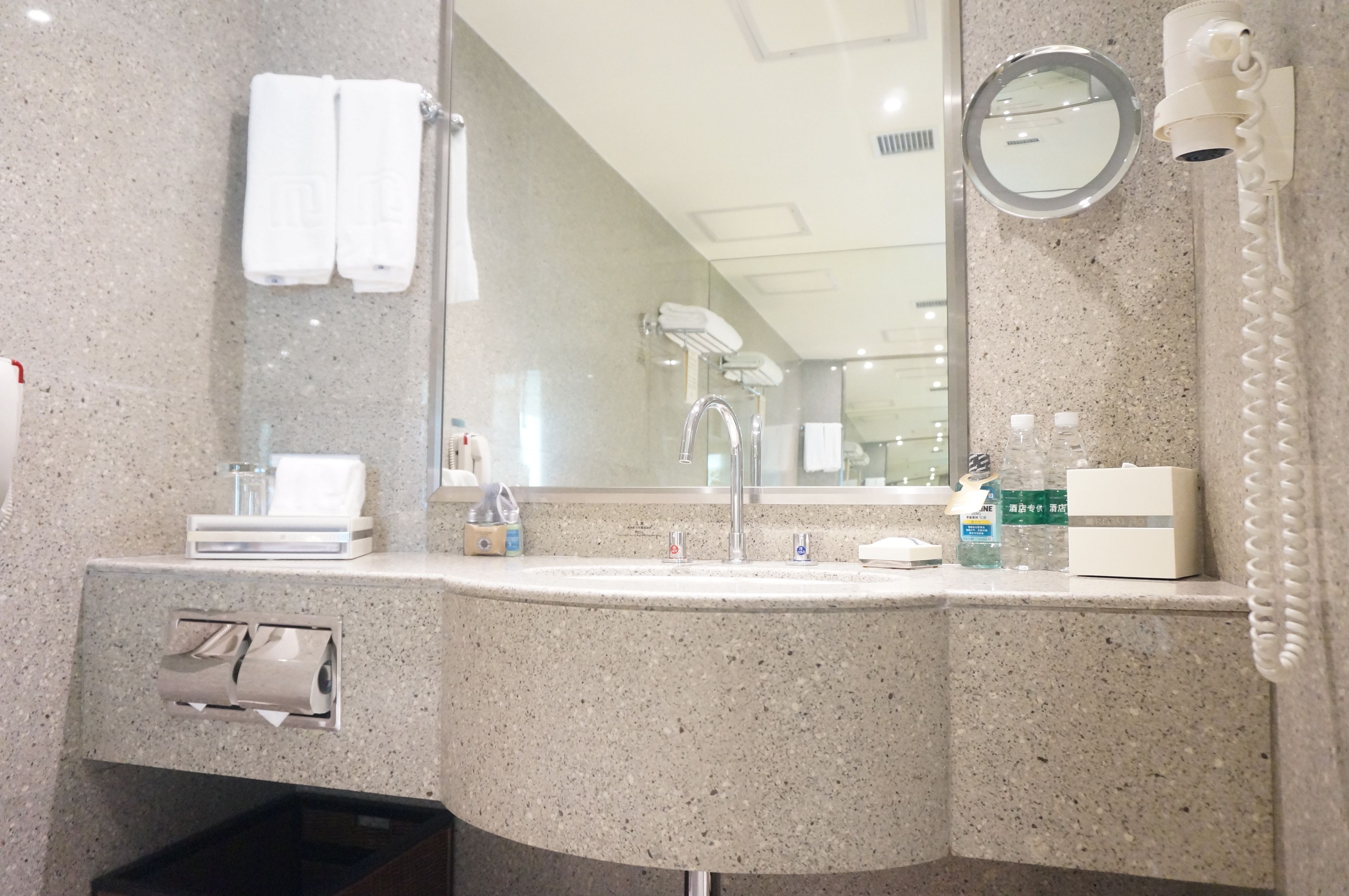 A bathroom with a granite countertop, a sink, a mirror, a towel rack, a hairdryer, and a trash bin.