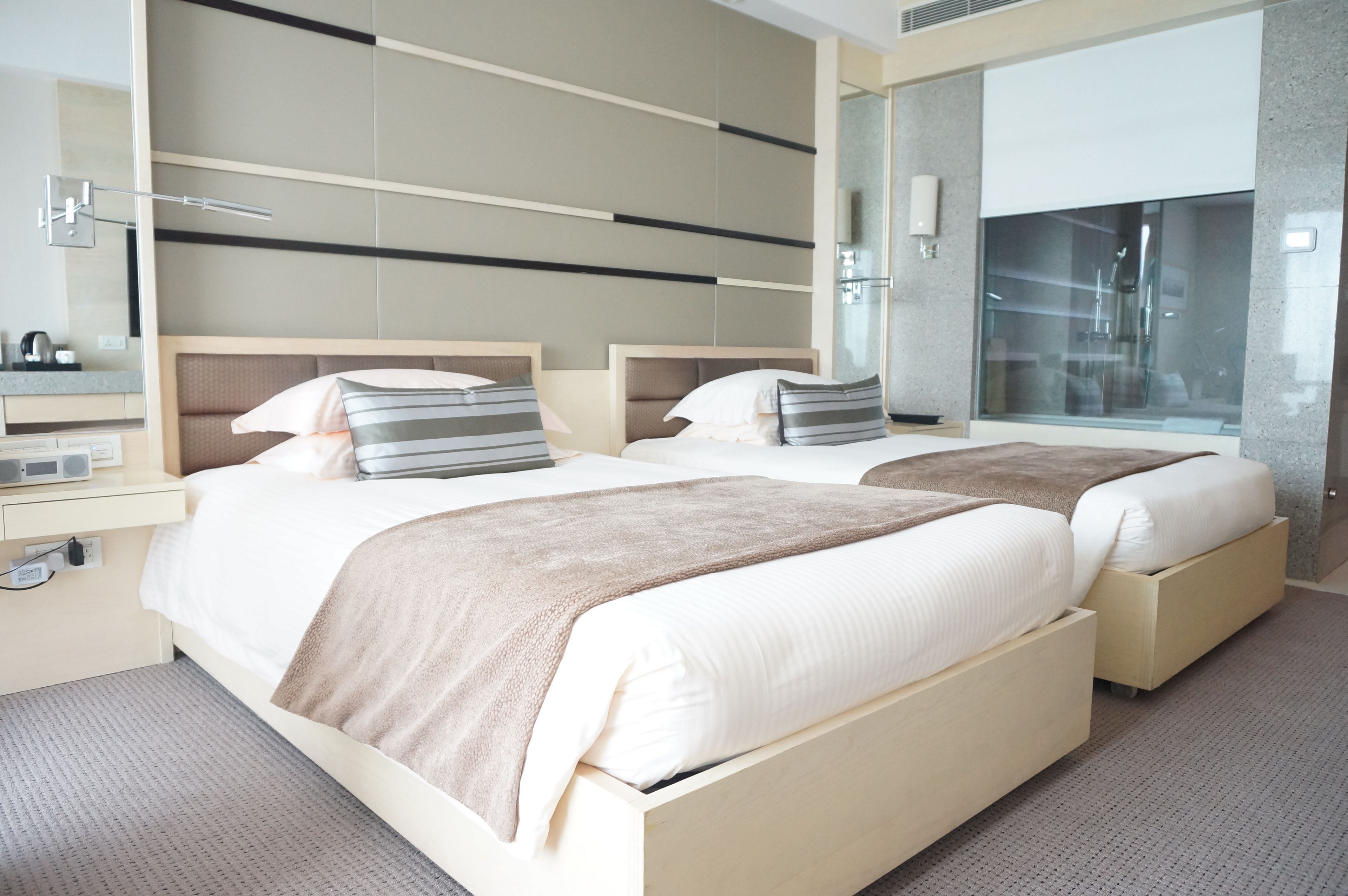 Habitació d'hotel moderna amb dos llits, un mirall gran i zona de banyera amb dutxa.