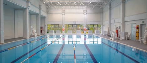 An indoor swimming pool with clear lanes, a high ceiling with metal beams, and windows providing natural light.