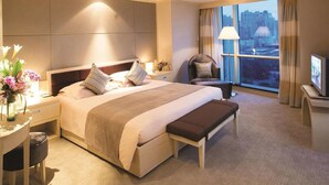 A hotel room with a large bed, bedside tables, a desk, a chair, a TV, and a window with a city view. - Hengshan Garden Hotel (Shanghai)