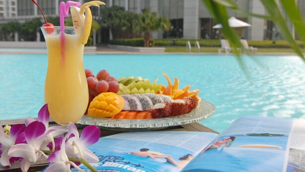 A fruit platter with a drink beside a pool, a magazine, and orchids. - Hainan Junhua Haiyi Hotel (Haikou)