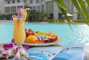 Una bandeja de frutas con una bebida junto a una piscina, una revista y orquídeas.