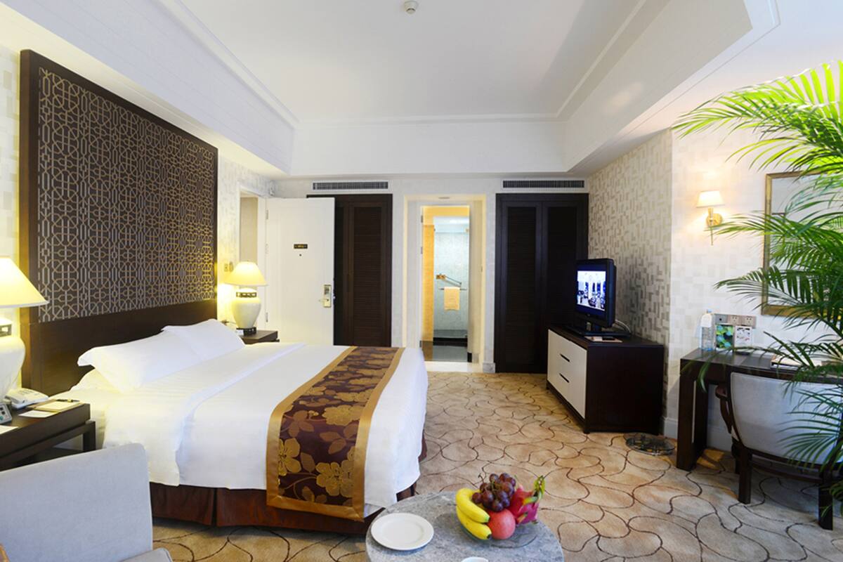 A hotel room with a bed, bedside table, TV, desk, chair, and a fruit bowl.