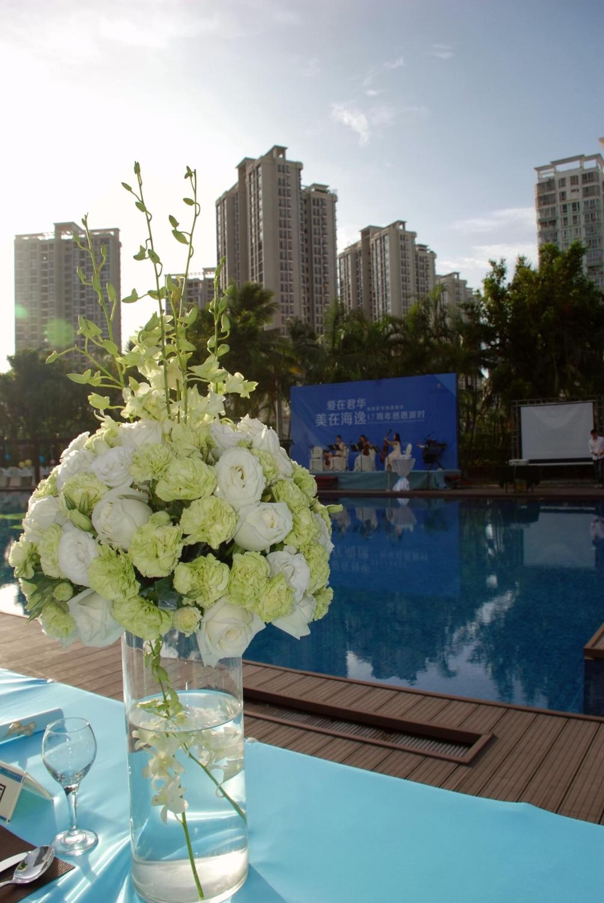 A table with a floral arrangement, a clear pool, and a cityscape in the background.