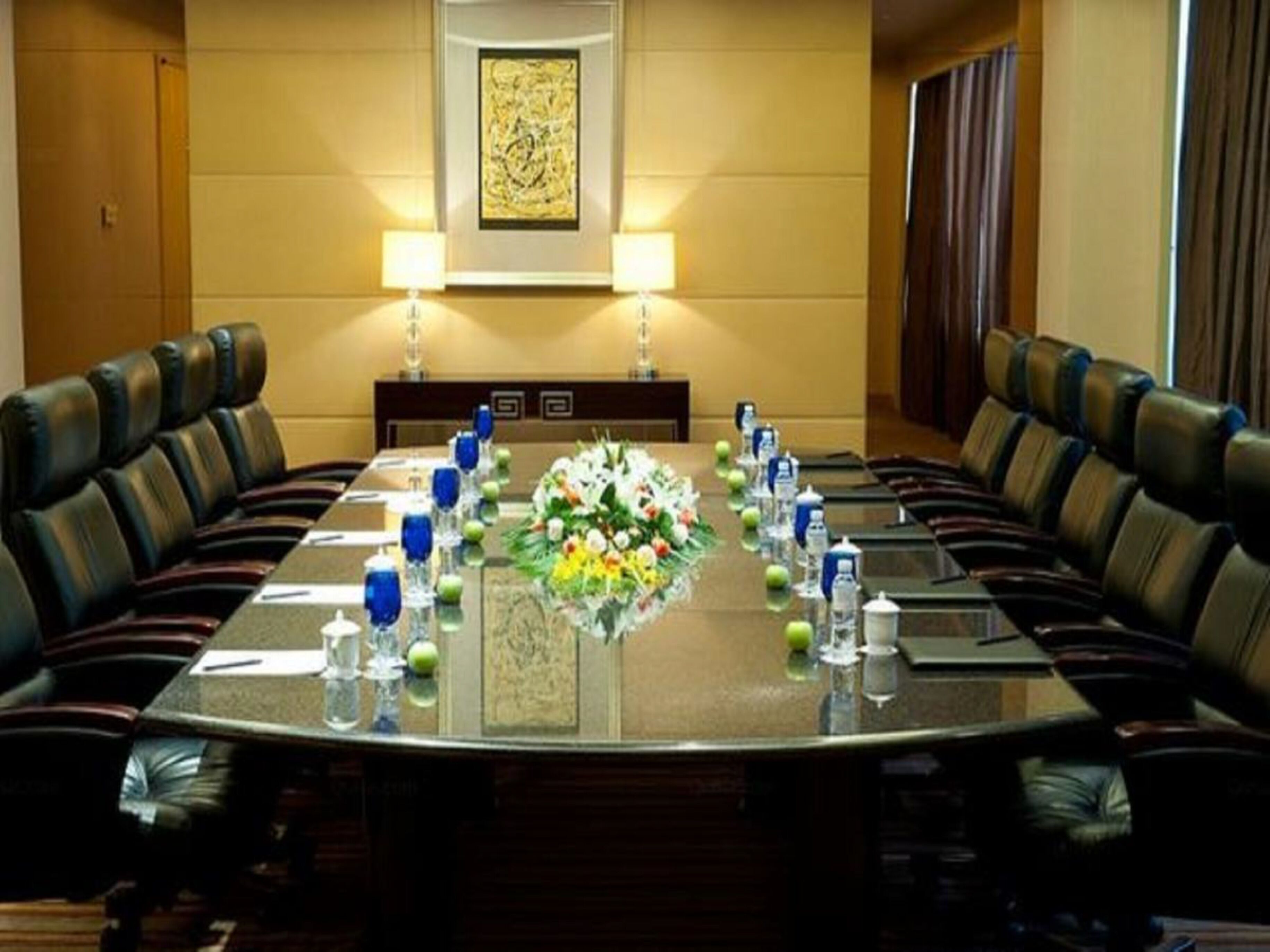Una sala de conferencias con una mesa larga, sillas de cuero, un centro de mesa floral y dos lámparas fijadas a la pared.