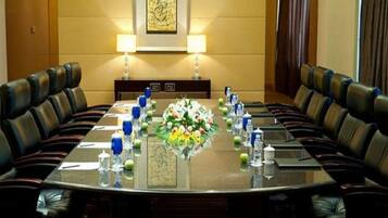 Una sala de conferencias con una mesa larga, sillas de cuero, un centro de mesa floral y dos lámparas fijadas a la pared.