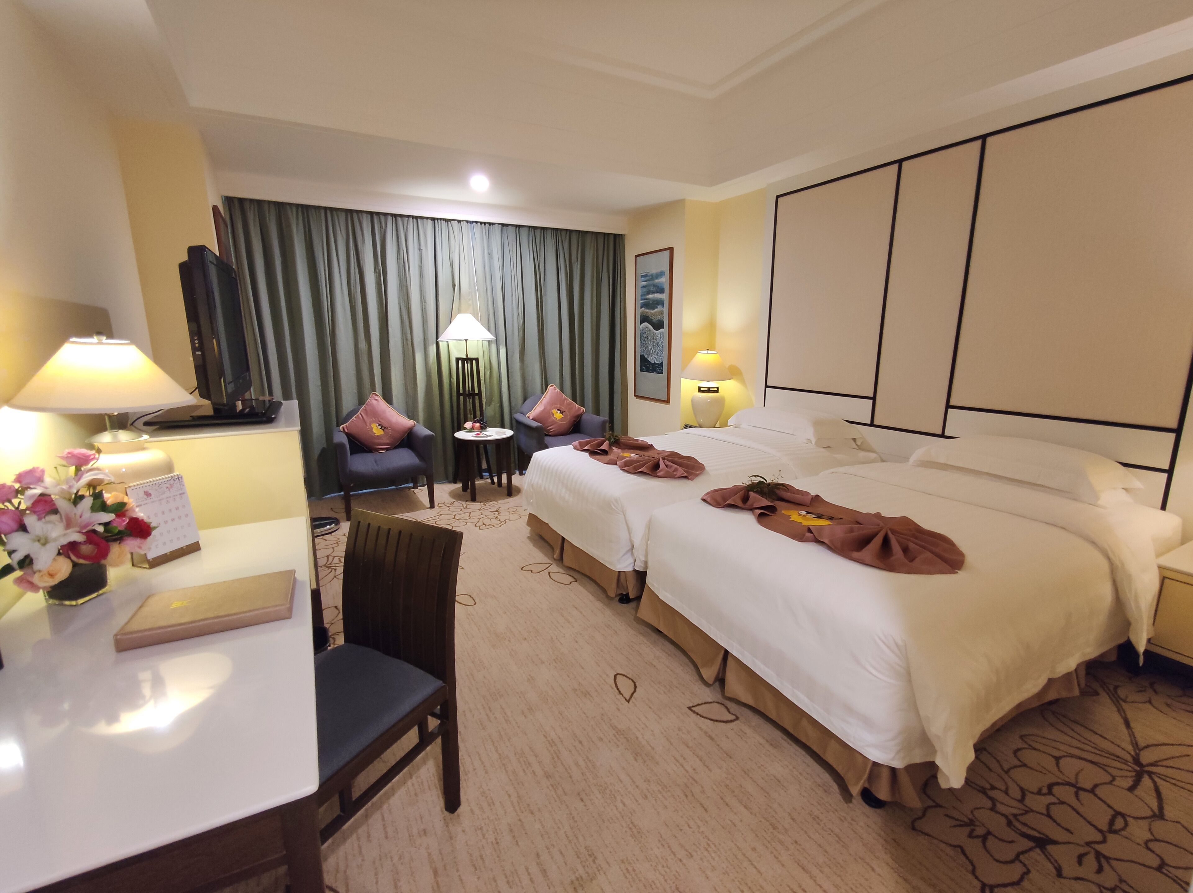 Una habitación de hotel con una cama grande, dos sillones, un escritorio con una lámpara y una mesita.