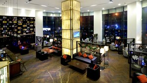A modern hotel lobby with a central seating area, a large bookshelf, and a view of the city through large windows. - Hainan Junhua Haiyi Hotel (Haikou)