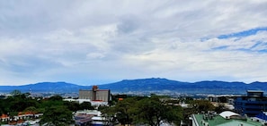 A cityscape with a prominent hotel building in the foreground, surrounded by trees and a mountainous backdrop. - Parque del Lago Boutique Hotel (San José)