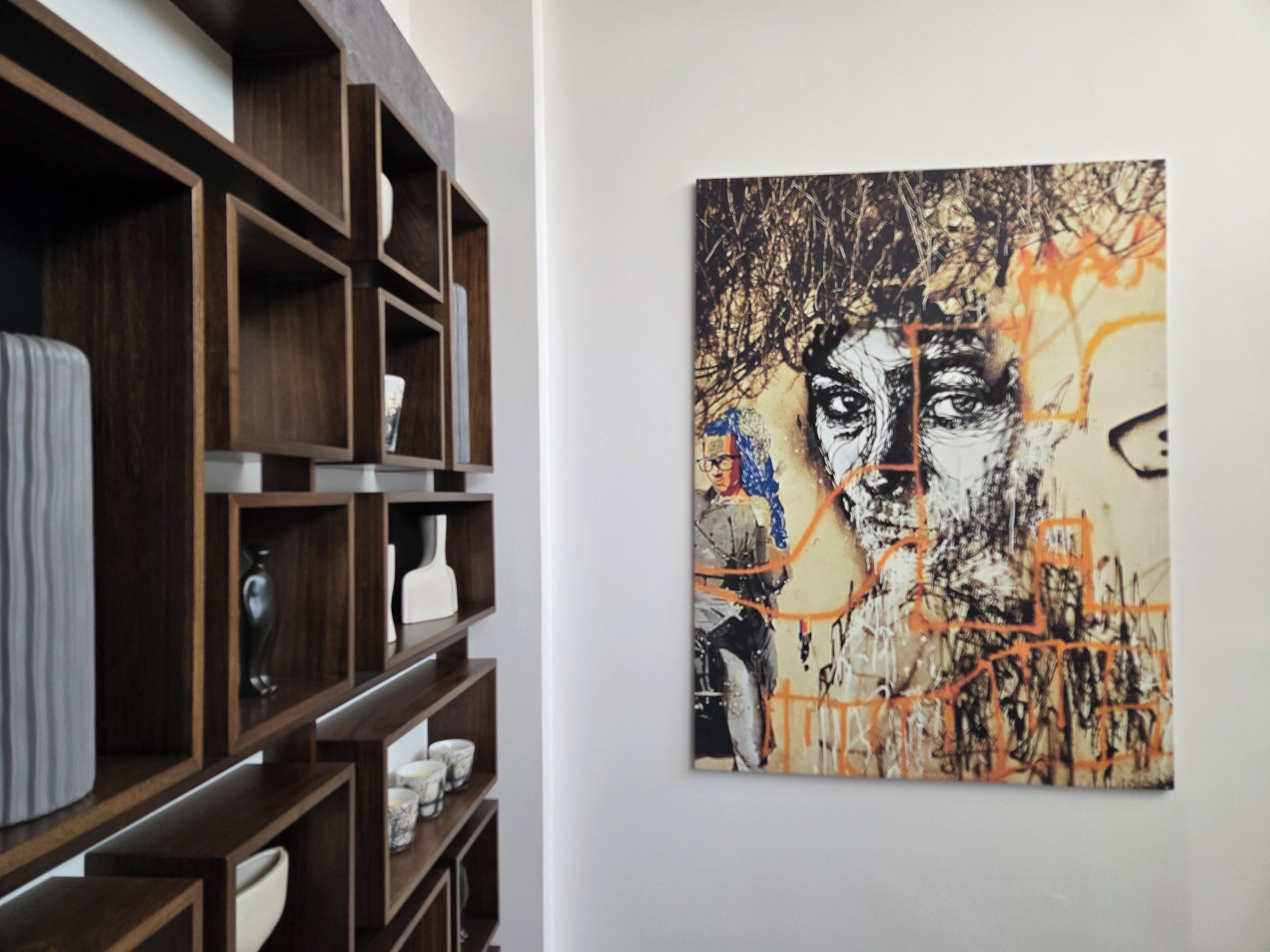 A room with a wooden shelving unit against a wall, a framed artwork, and a white door.