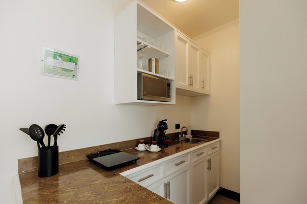 A kitchen with white cabinets, a microwave, a coffee maker, and a knife block. - Parque del Lago Boutique Hotel (San José)
