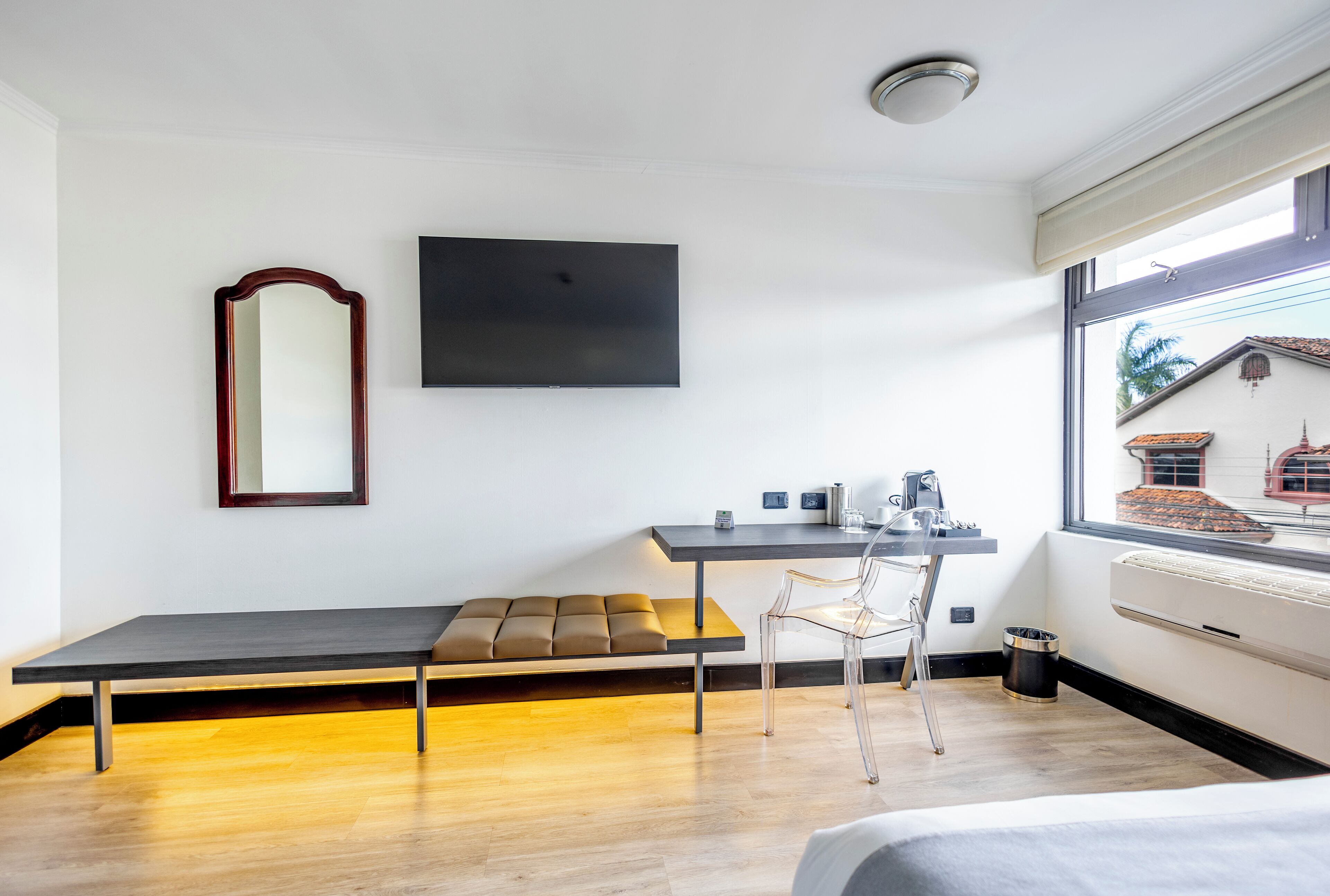 A modern room with a bed, a desk with a chair, a large mirror, and a TV.