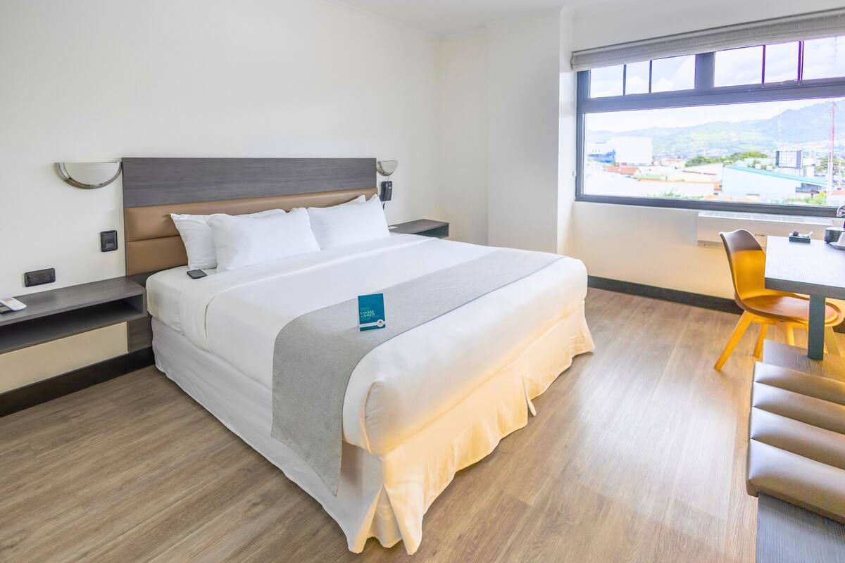 A hotel room with a bed, bedside tables, a desk, and a chair.