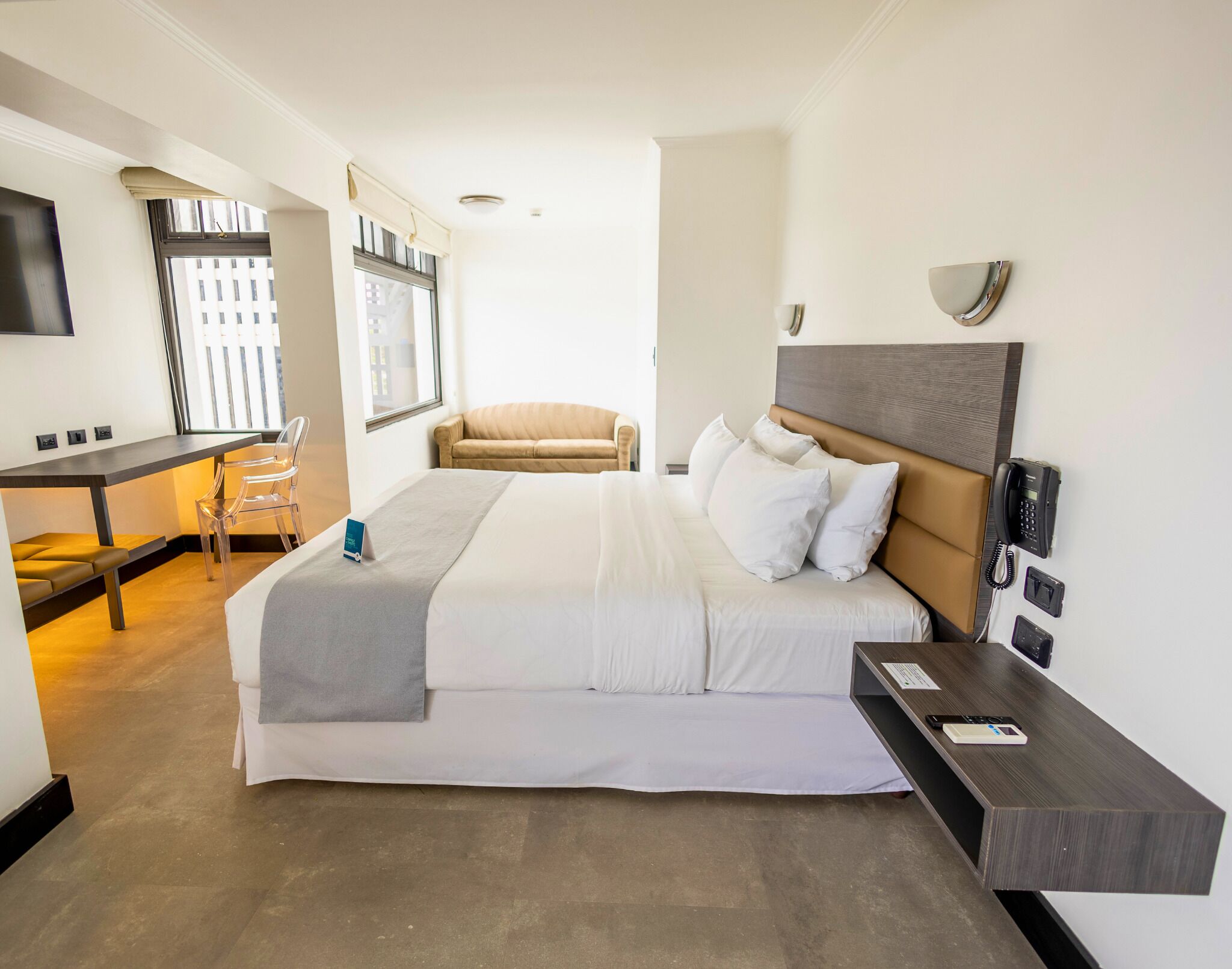 A hotel room with a bed, bedside table, desk, and chair.