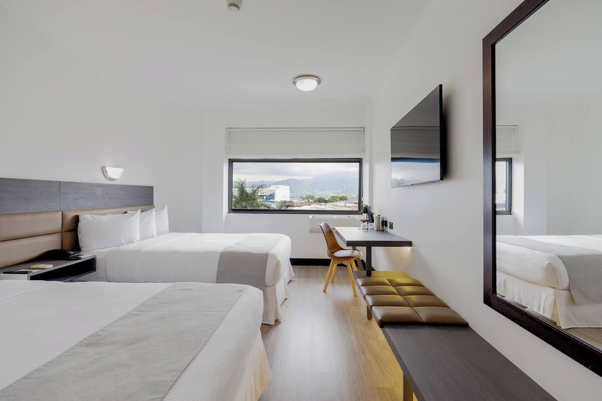 A modern hotel room with two beds, a desk, a chair, and a large mirror.