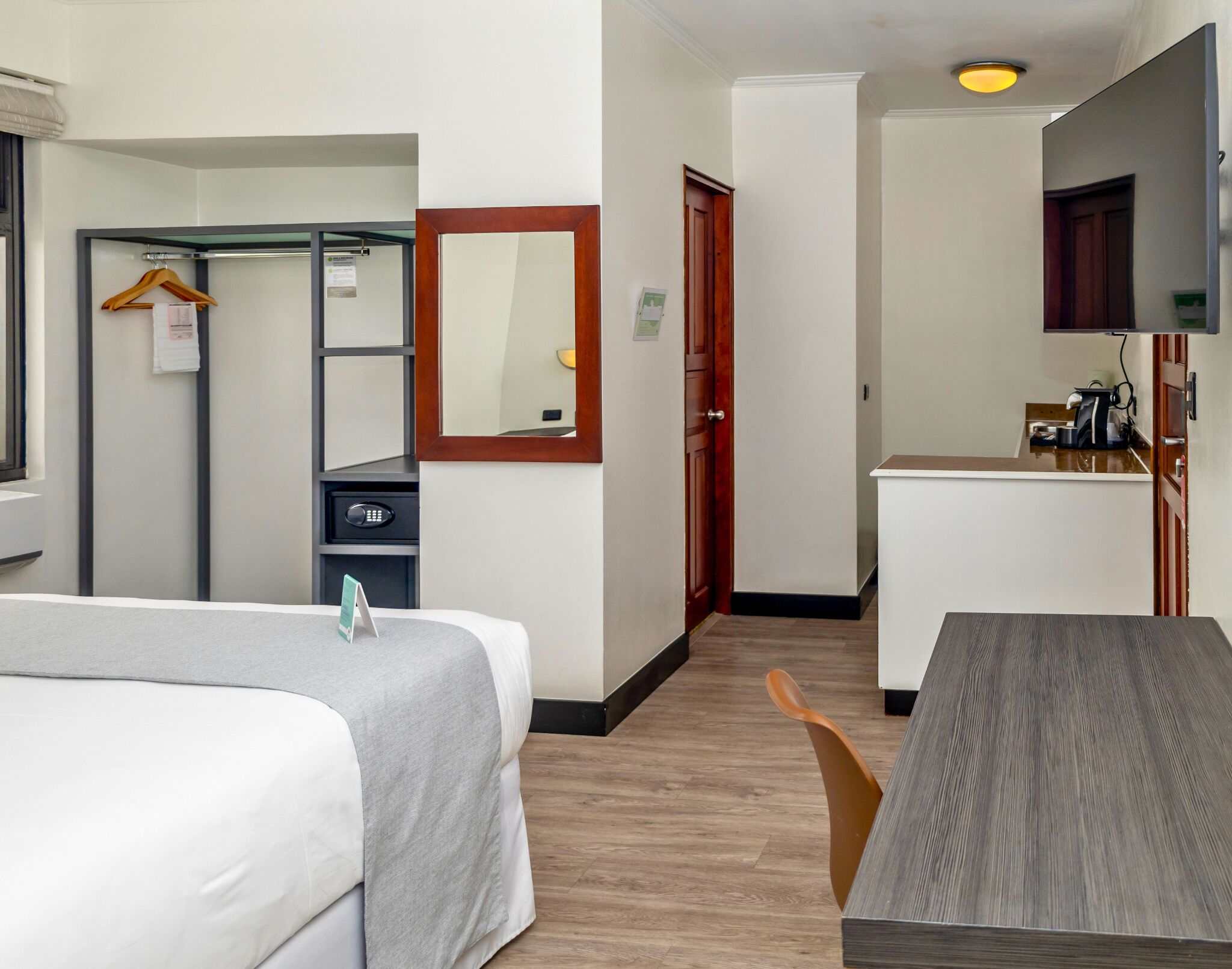A hotel room with two beds, a small kitchenette, a mirror, and a wooden floor.