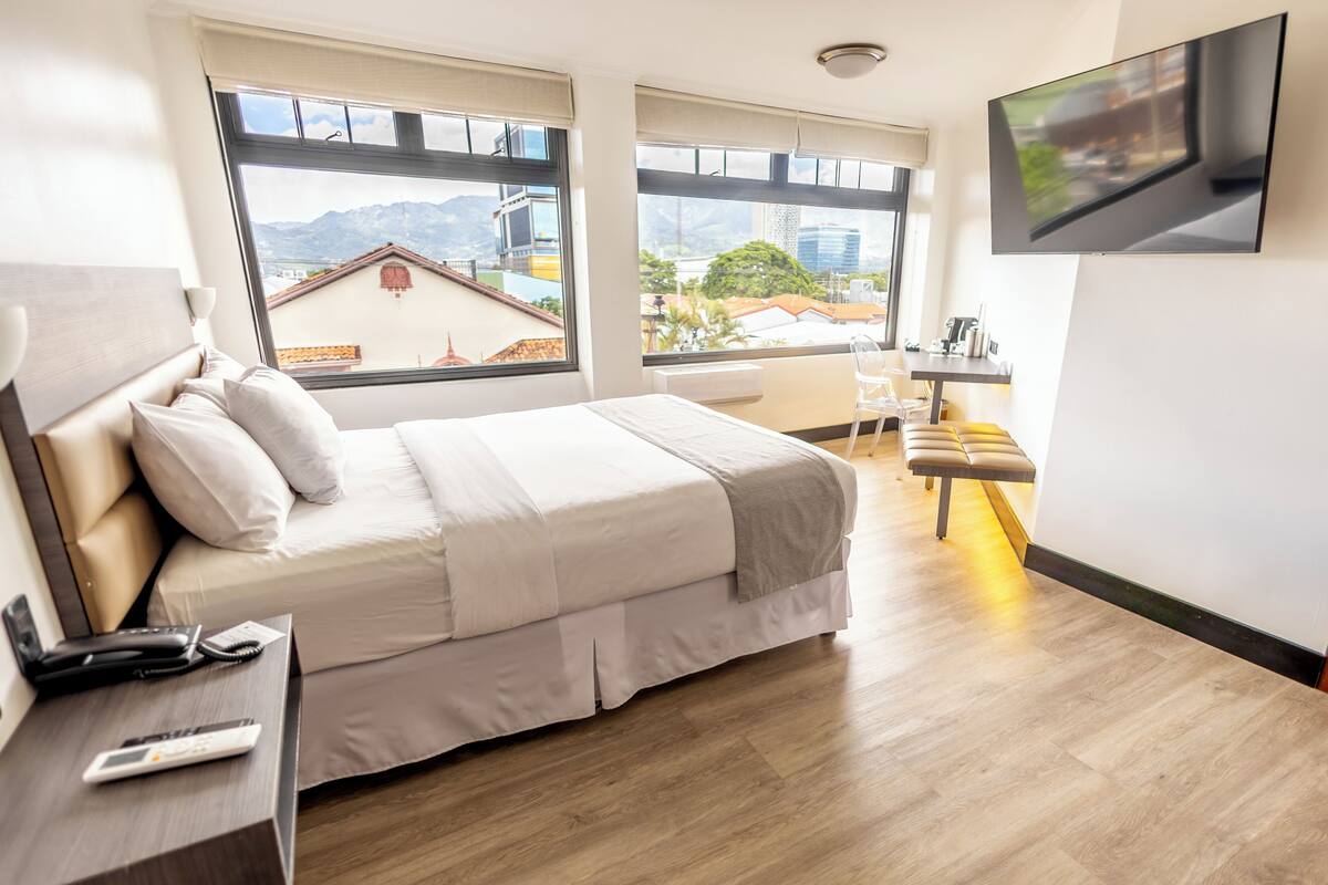 A hotel room with a bed, bedside table, TV, and a desk with a chair.