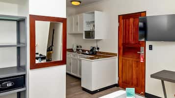 A compact hotel room with a kitchenette, a wooden door, a TV mounted on the wall, and a small table.