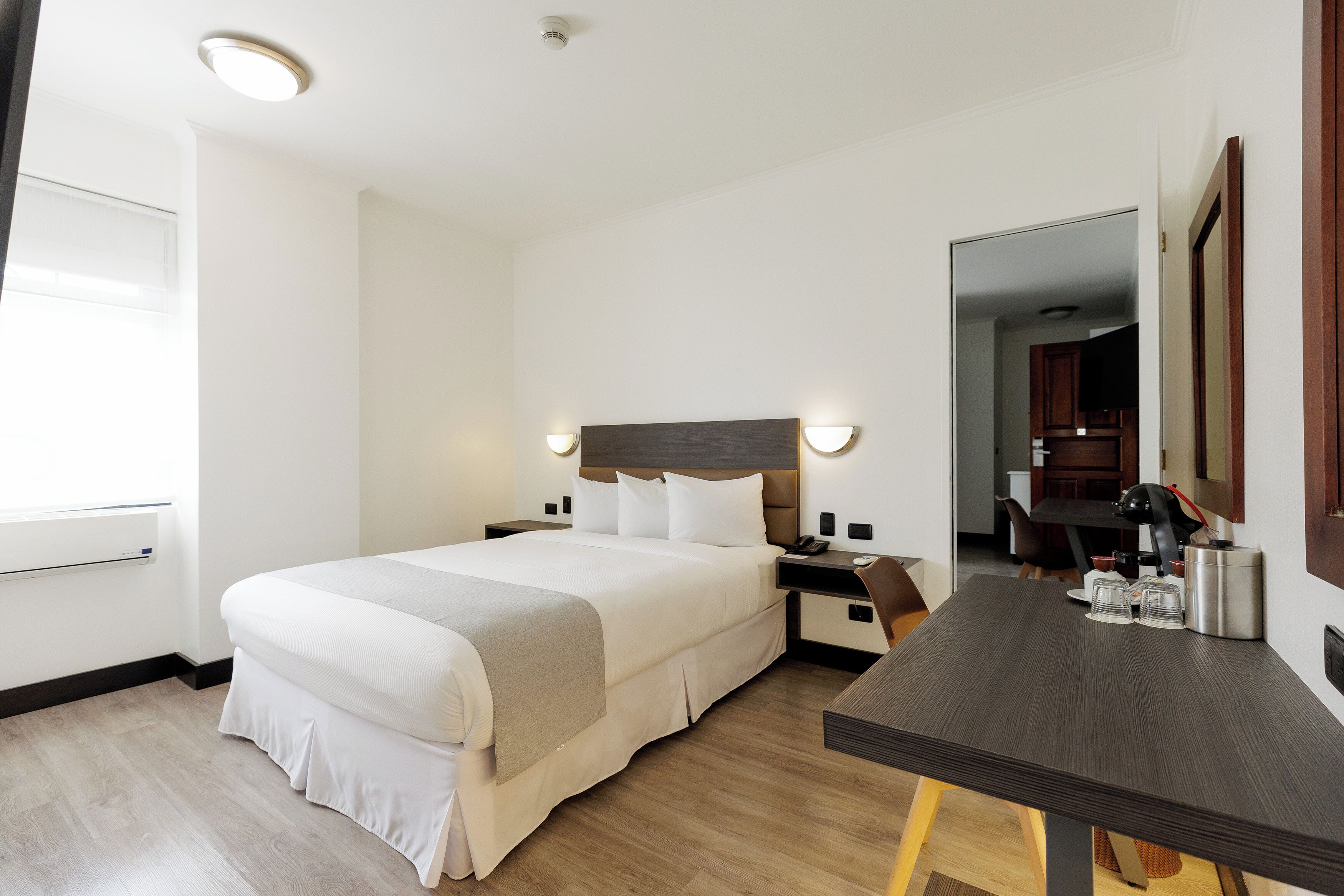 A hotel room with a large bed, bedside tables, a desk, and a mirror.