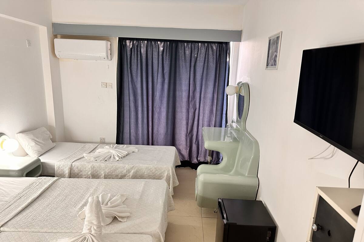 A hotel room with two beds, a TV, a desk, and a bathroom mirror.