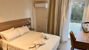 Hotellihuone, jossa on sänky, puinen pääty, yöpöytä, ilmastointilaite, ikkuna verhoilla ja näkymä ulos.