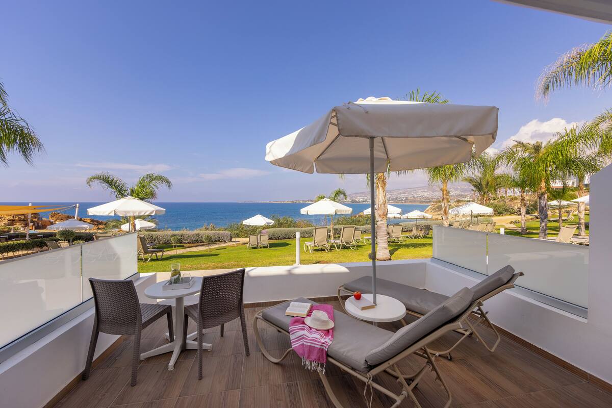A balcony with a view of the sea, furnished with a table, chairs, and a lounge chair.
