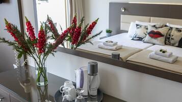 A hotel room with a bed, a bedside table with a vase of red flowers, a tray with toiletries, and a large mirror reflecting the room.