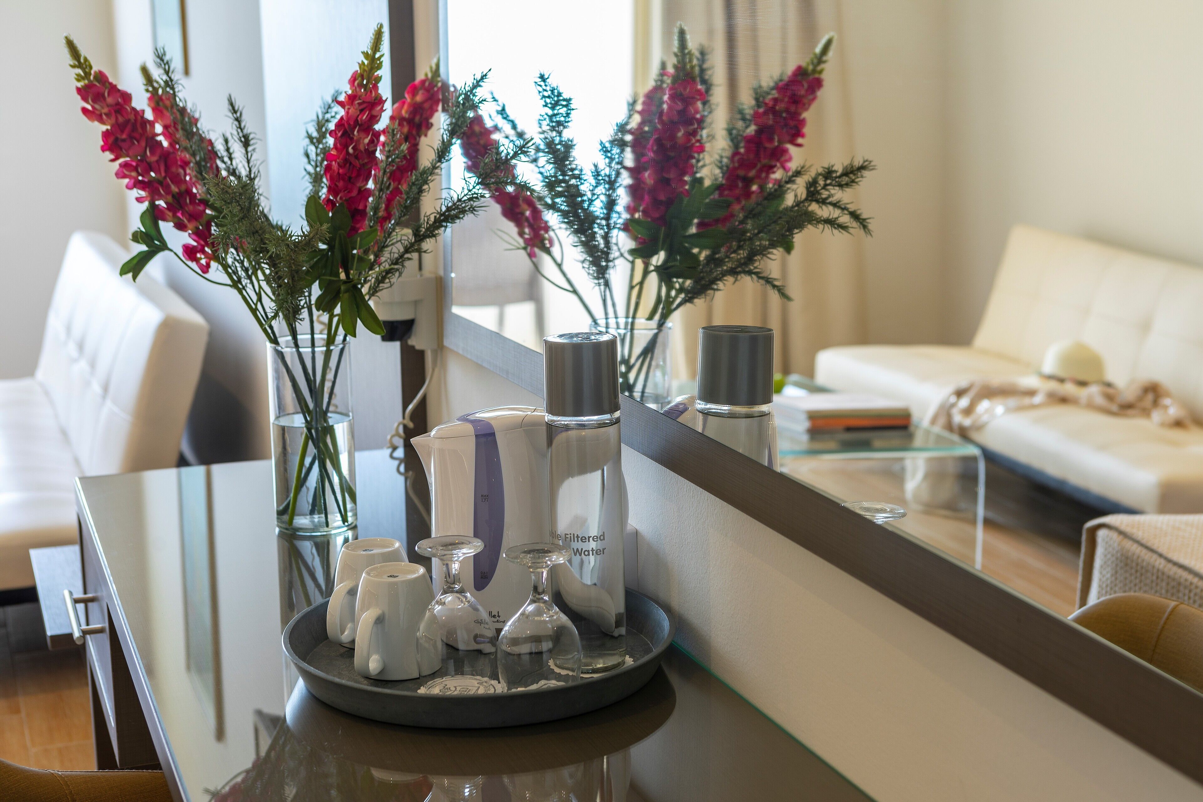 Ein modernes Wohnzimmer mit einem Glastisch, einem weißen Sofa und dekorativen Blumen in Glasvasen.