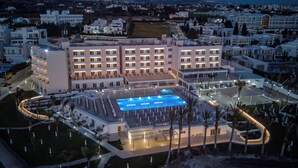 A modern hotel with multiple floors, a swimming pool, and a landscaped garden. - Queen's Bay Hotel (Kissonerga)