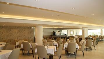 A spacious dining area with multiple tables and chairs, a central bar, and a stone wall.