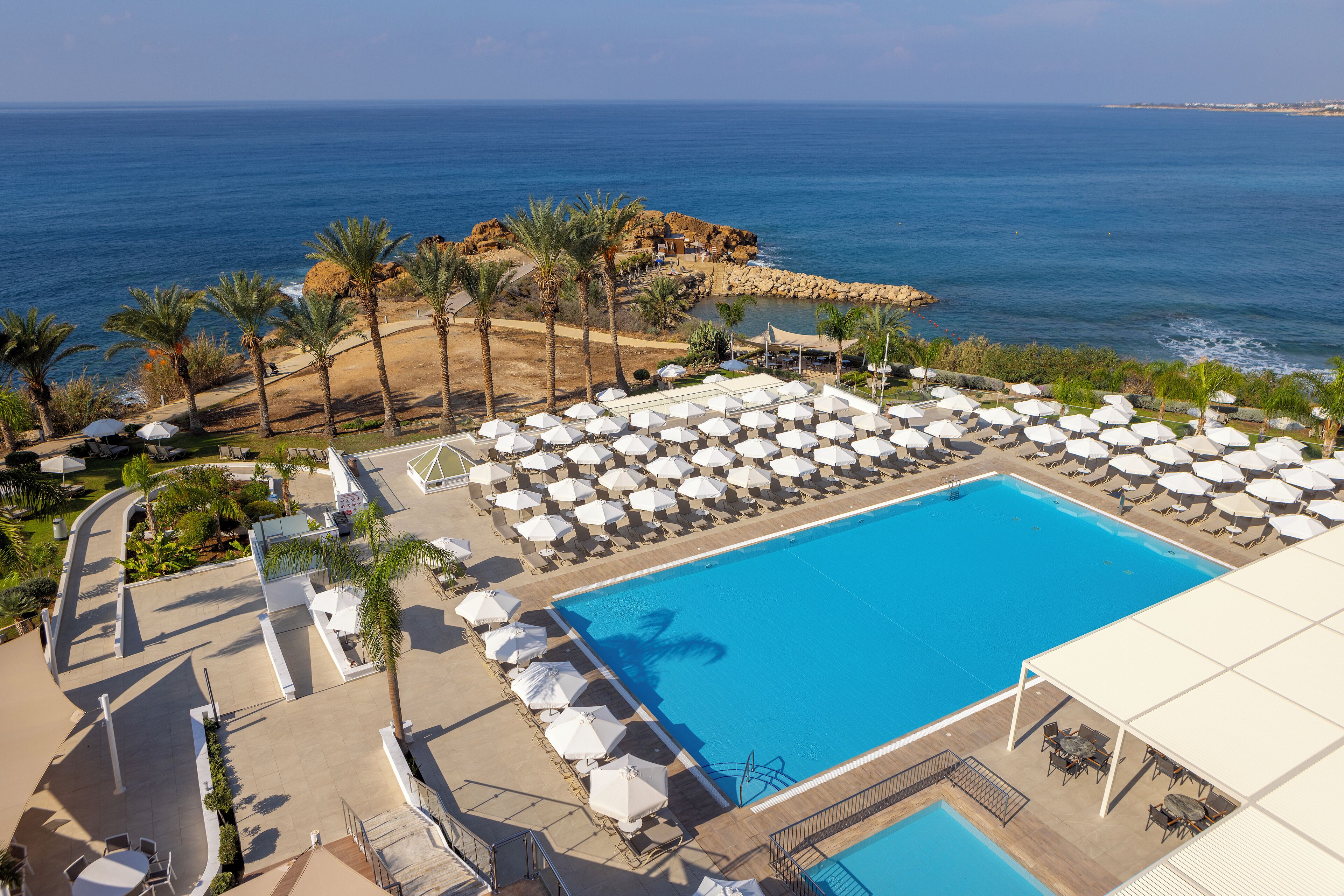 Un complexe hôtelier doté d’une grande piscine, de chaises longues, de parasols et offrant une vue sur l’océan.