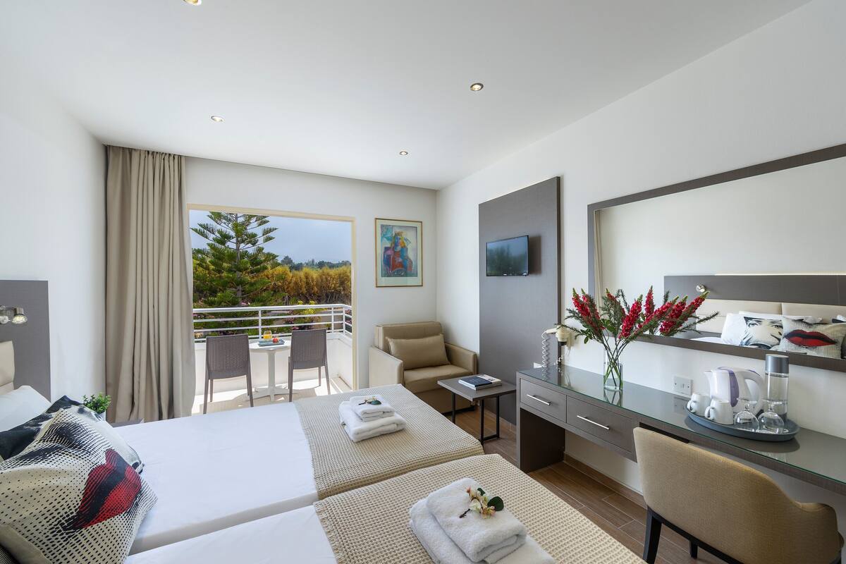 A hotel room with two beds, a desk, a chair, a balcony with a view, and a TV.